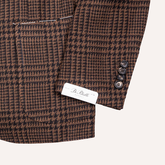 Close-up of a brown and black houndstooth patterned blazer sleeve with three dark buttons and a white brand label reading Dr. Belle.