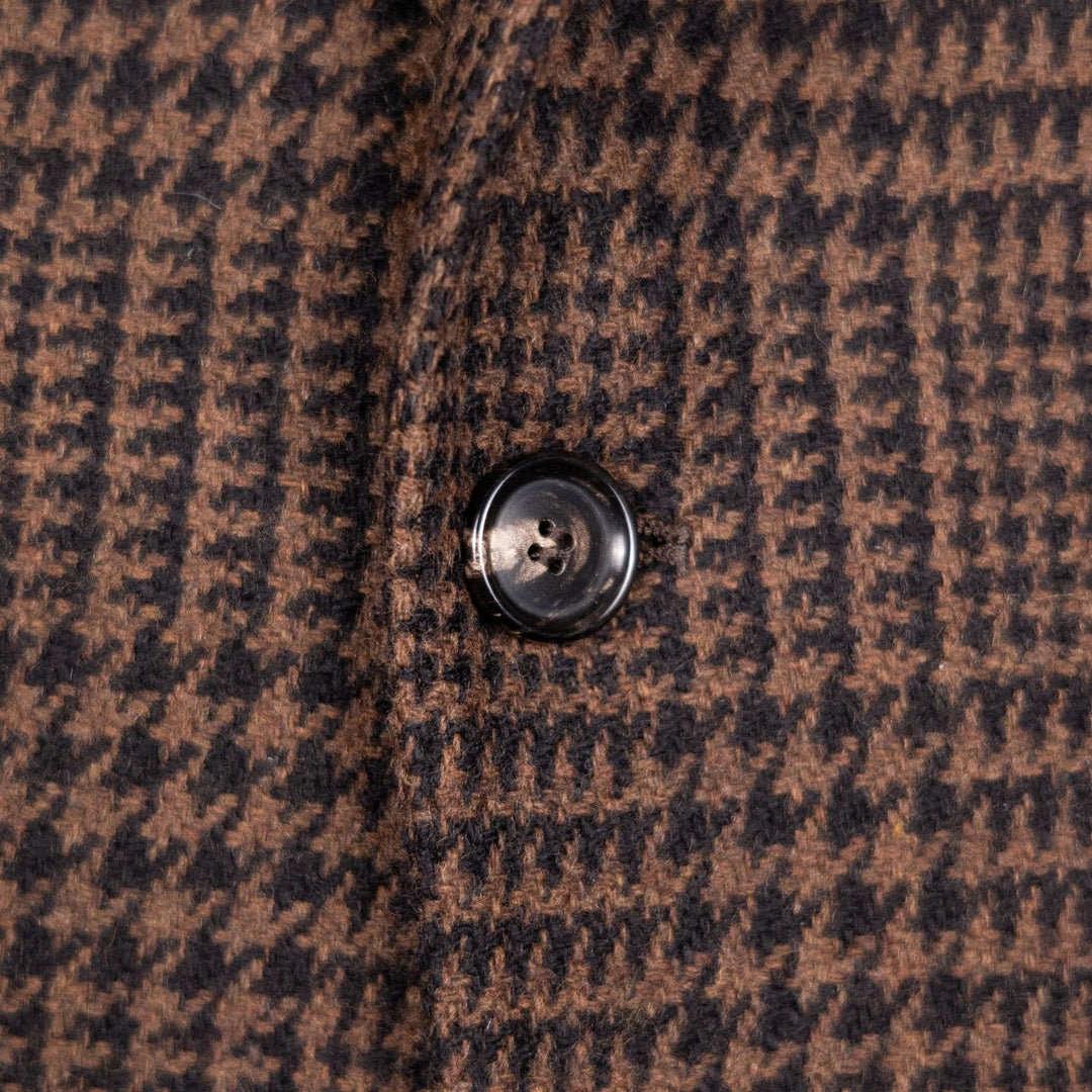 Close-up of a brown and black houndstooth patterned fabric with a single dark button on the left side.