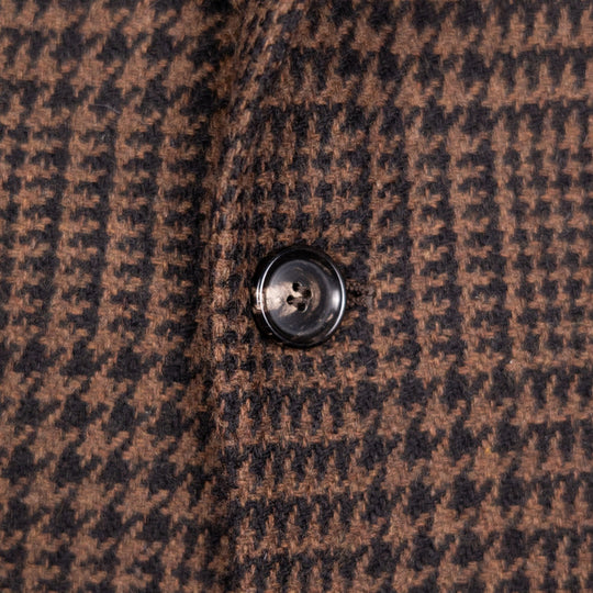 Close-up of a brown and black houndstooth patterned fabric with a single dark button on the left side.