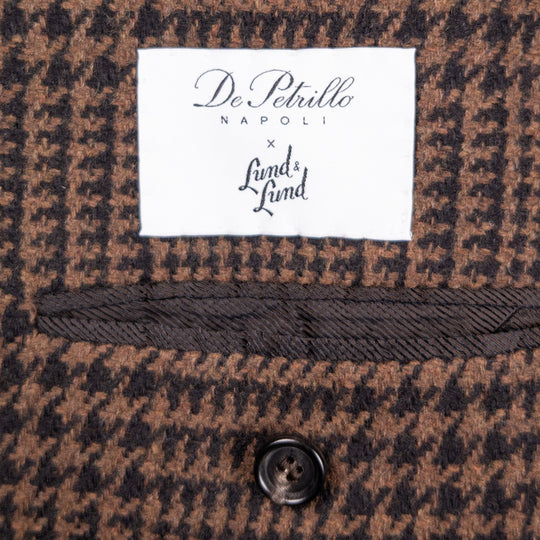 Close-up of a brown and black houndstooth patterned textile with a white woven label reading 'De Petrillo NAPOLI x Lund & Lund' and a dark button below.
