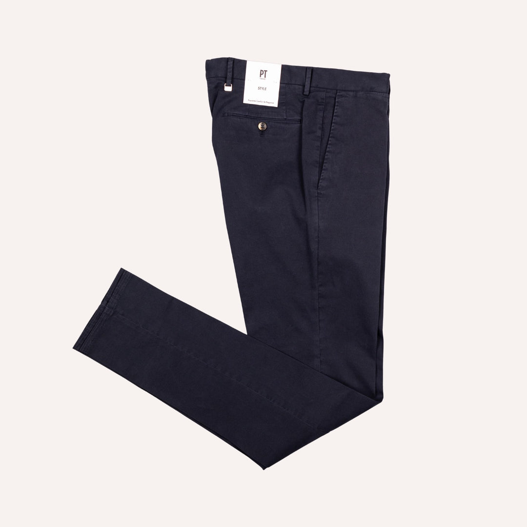 A pair of dark navy blue chino pants folded neatly on a light cream background, with a white brand tag visible at the waistband.