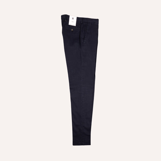 A pair of dark navy blue slim-fit trousers shown flat against a light cream background, with a small white brand tag visible at the waistband.