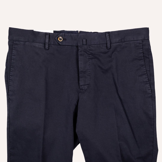 A close-up of dark navy blue trousers showing the waistband, belt loops, button closure, and front pocket on a light off-white background.