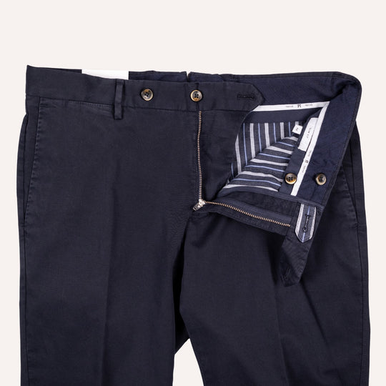 Close-up of dark navy trousers showing the front waistband, button closure, zipper, and interior striped lining on a light beige background.