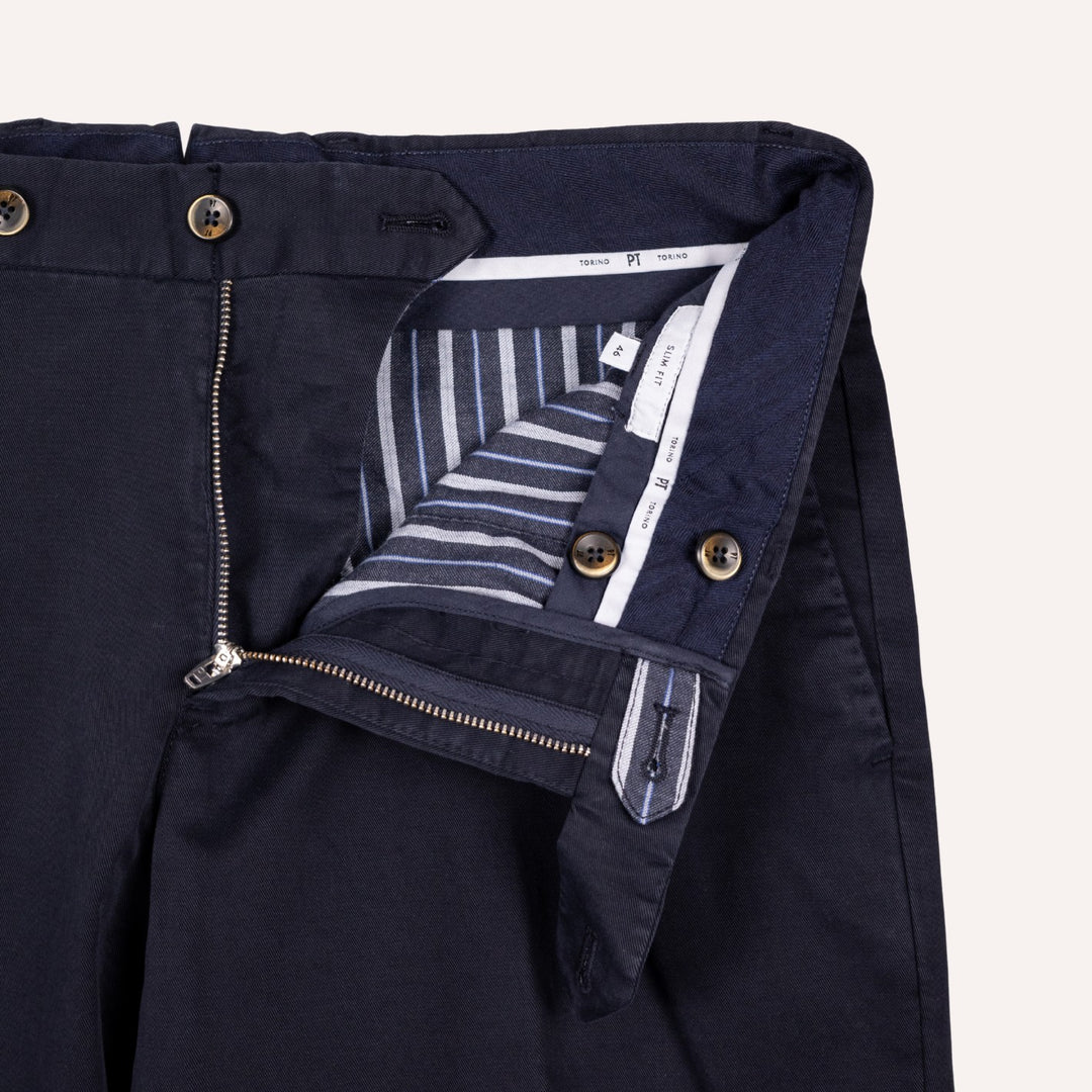 Close-up of dark navy trousers showing the waistband, front zipper, button closure, and striped inner lining.