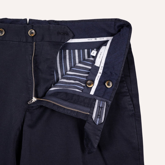 Close-up of dark navy trousers showing the waistband, front zipper, button closure, and striped inner lining.