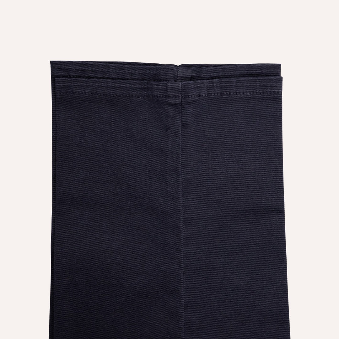 Close-up of folded dark navy blue denim fabric, showing the texture and stitching, on a light off-white background.