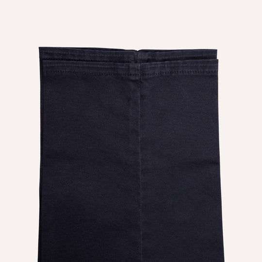 Close-up of folded dark navy blue denim fabric, showing the texture and stitching, on a light off-white background.