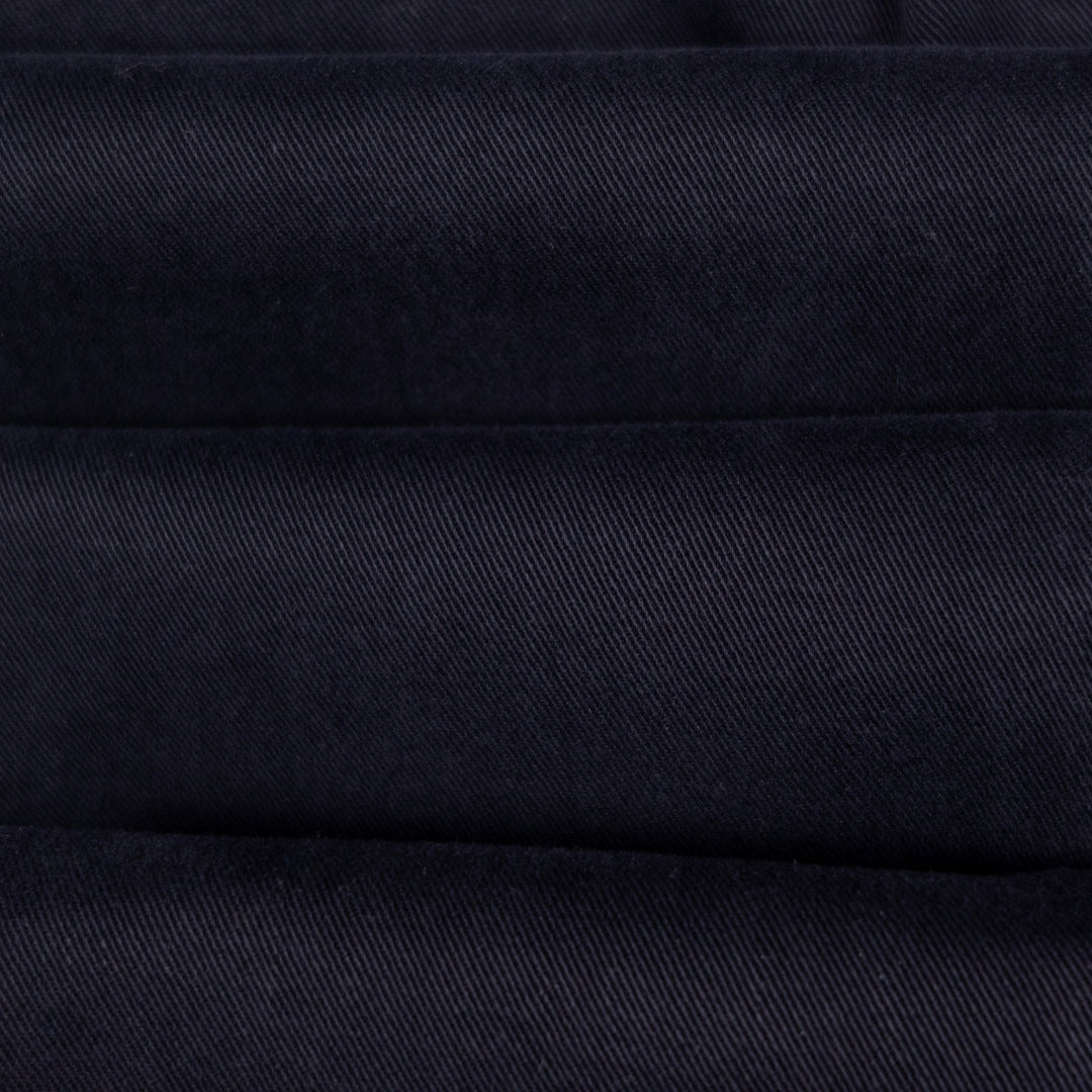 A close-up of dark navy blue fabric with a fine diagonal twill texture and horizontal stitched seams.