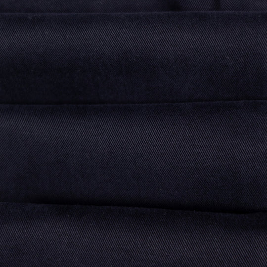 A close-up of dark navy blue fabric with a fine diagonal twill texture and horizontal stitched seams.