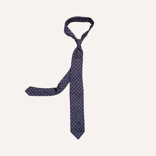 A navy blue necktie with a small taupe flower dot pattern, neatly knotted and displayed against a solid off-white background.