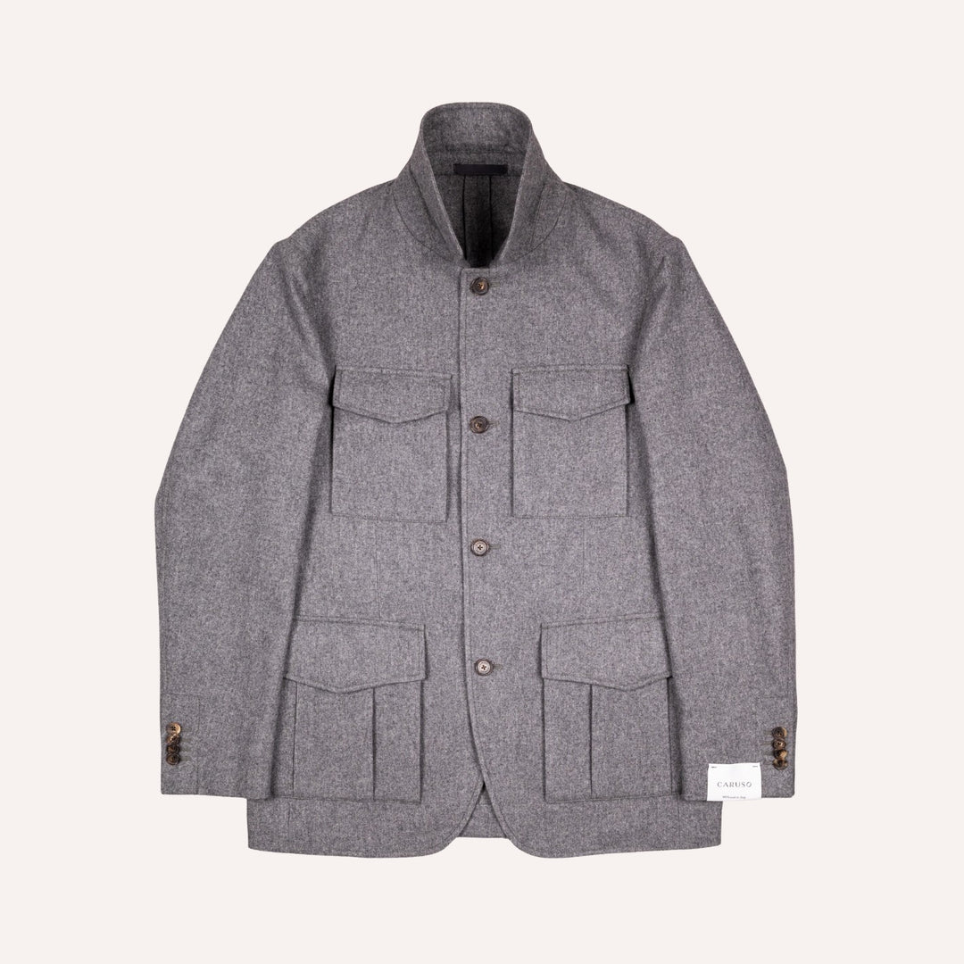 A gray textured wool jacket with a stand collar, button closure, and four front flap pockets, displayed flat against a light cream background.