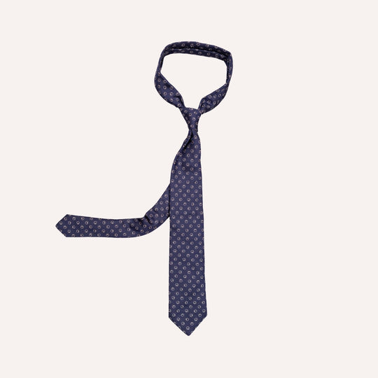 A navy blue necktie with a repeating small white geometric pattern, styled in a knot on a solid off-white background.