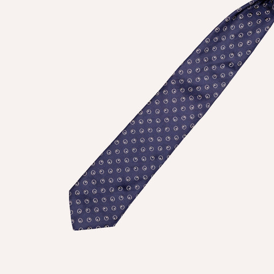 A navy blue silk necktie with a repeating white anchor pattern, shown diagonally on a light cream background.