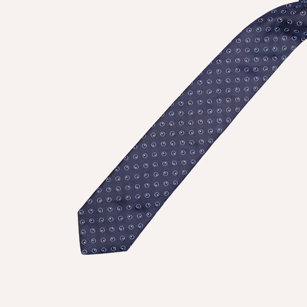 A navy blue necktie with a repeating small white and light blue circular dot pattern, shown diagonally on a solid off-white background.