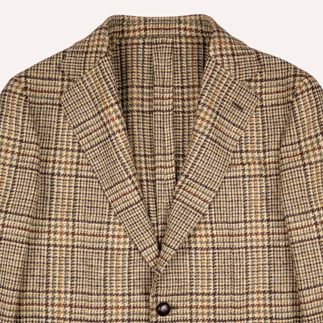 Close-up of a tweed blazer with a brown, beige, and black windowpane plaid pattern, featuring a single dark button and notch lapels.