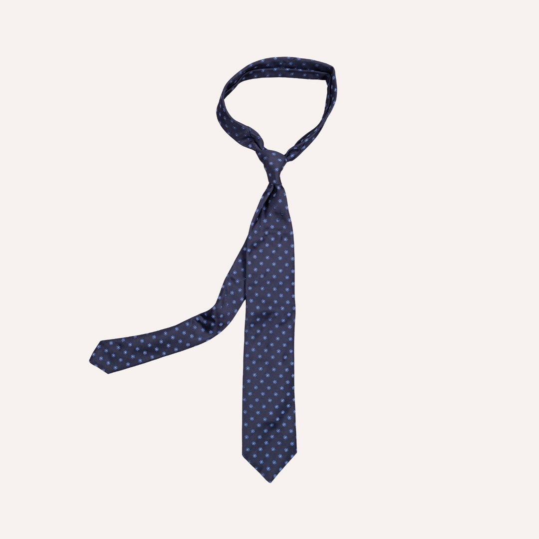 A navy blue necktie with a small light blue polka dot pattern, shown tied in a standard knot on a solid off-white background.