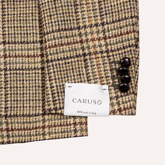 Close-up of a Caruso woven fabric with a subtle houndstooth pattern in beige, brown, and olive green, featuring three dark buttons and a white brand label.