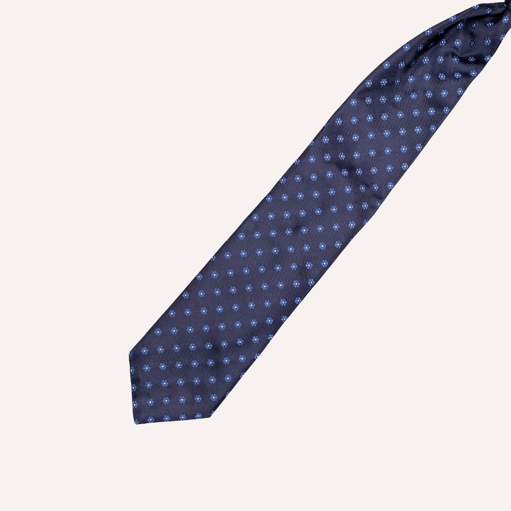 A navy blue necktie with a repeating small light blue floral pattern, laid diagonally on a solid off-white background.