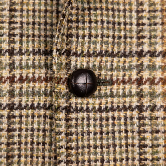 Close-up of a textured tweed fabric with a black button, showing a woven pattern of beige, brown, and muted green.