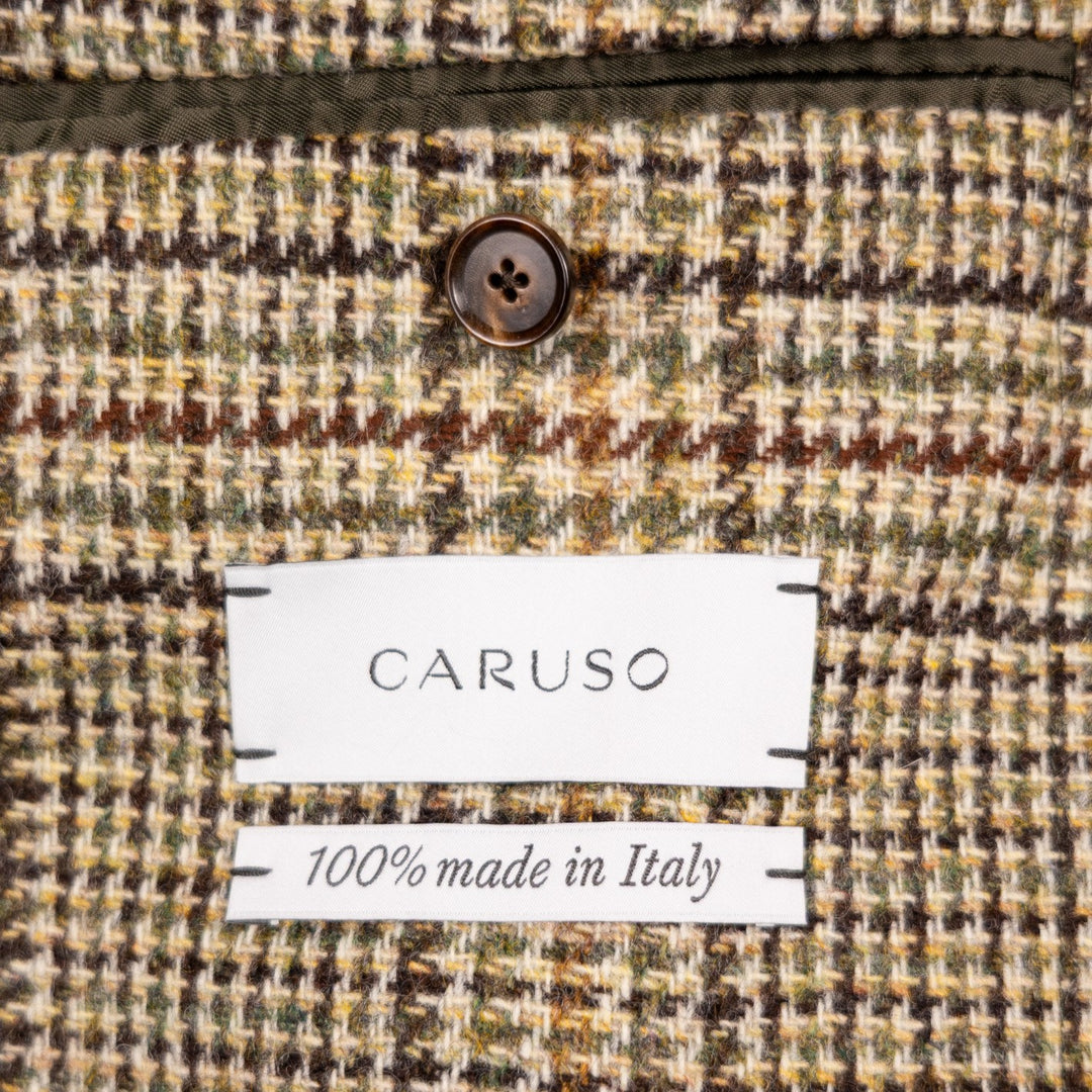 Close-up of a textured woven fabric with a visible CARUSO label and '100% made in Italy' text, showing a multicolor houndstooth-like pattern in beige, brown, olive green, and cream.