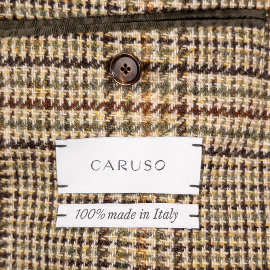 Close-up of a textured woven fabric with a visible CARUSO label and '100% made in Italy' text, showing a multicolor houndstooth-like pattern in beige, brown, olive green, and cream.
