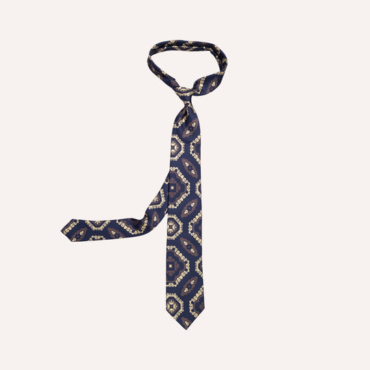 A navy blue necktie with a beige and taupe geometric pattern, knotted and displayed against a solid off-white background.