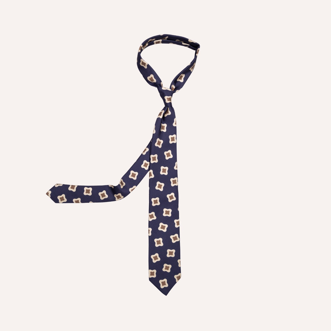 A navy blue necktie with a repeating beige and white geometric pattern, displayed on a solid off-white background.