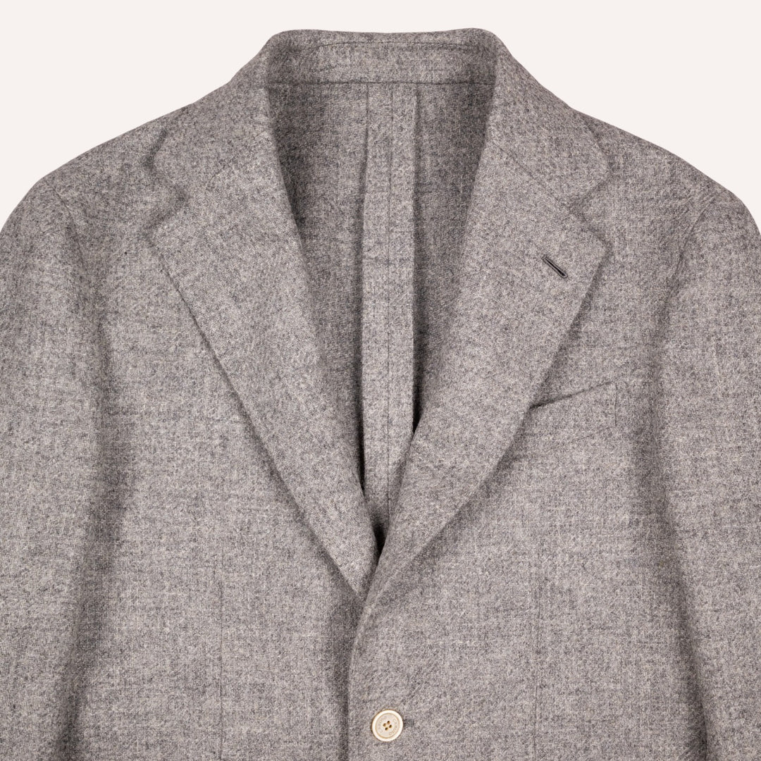 Close-up of a gray textured wool blazer jacket showing the collar, lapels, and a single button closure on a light off-white background.
