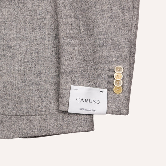 Close-up of a gray wool-blend blazer sleeve showing the cuff, three light wood buttons, and a white CARUSO brand label sewn onto the inside of the cuff.