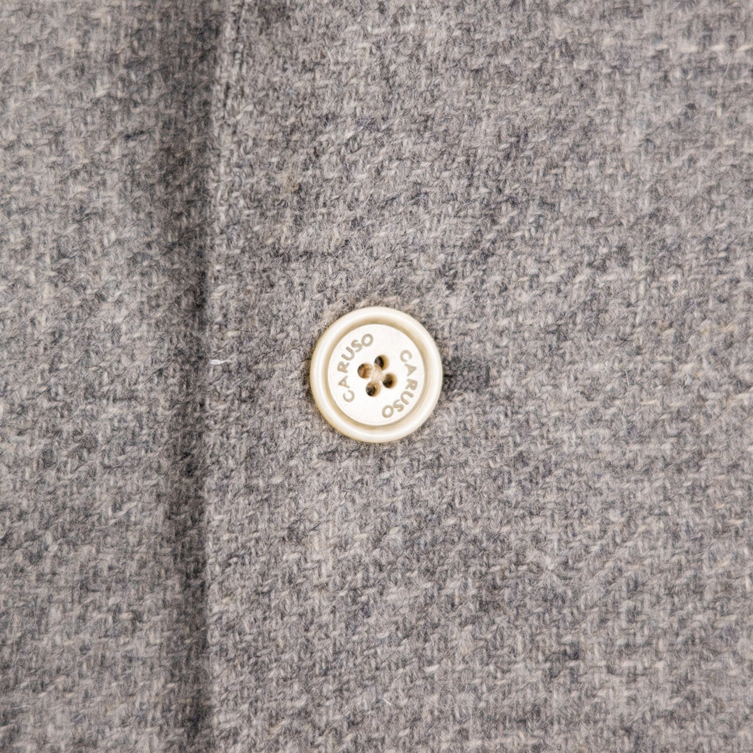 Close-up of a gray textured fabric with a round cream-colored button printed with the brand name 'CARUSO'.