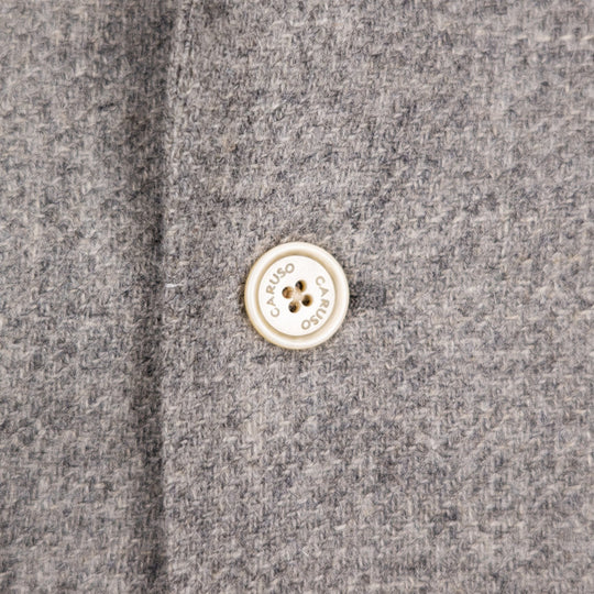 Close-up of a gray textured fabric with a round cream-colored button printed with the brand name 'CARUSO'.