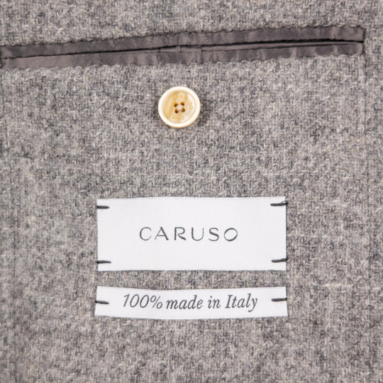 Close-up of a gray textured fabric surface with a white CARUSO label and a second label reading '100% made in Italy', plus a small cream button above.
