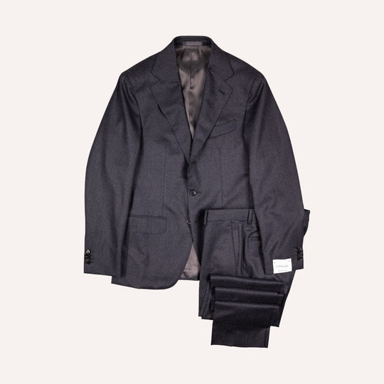 A dark charcoal gray two-piece suit consisting of a single-breasted blazer and matching trousers, neatly folded and displayed against a solid off-white background.
