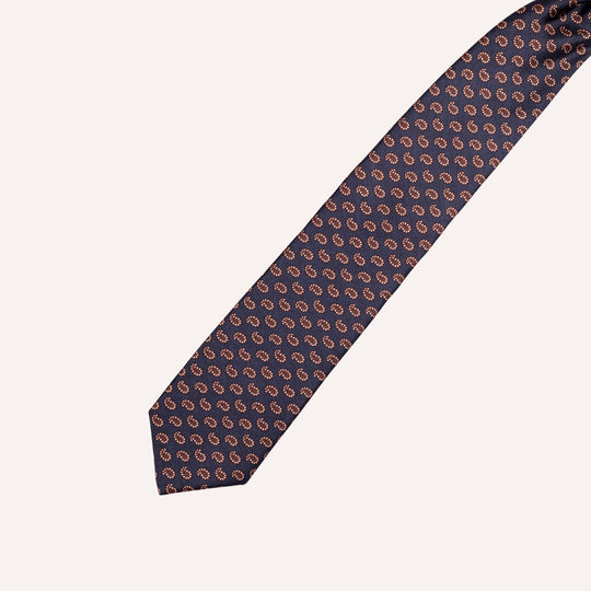 A classic necktie with a repeating paisley pattern in brown and white on a dark navy blue background, laid out diagonally on a light cream background.