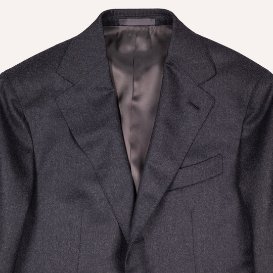 A close-up of a dark charcoal gray textured wool-blend suit jacket with a satin gray inner lining, shown against a plain off-white background.