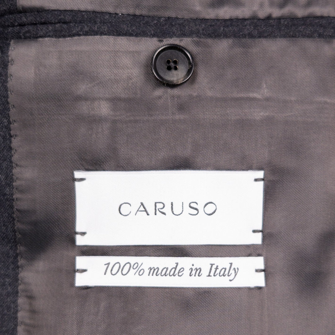 Close-up of a dark gray garment interior with a visible CARUSO label reading '100% made in Italy' and a dark button above it.