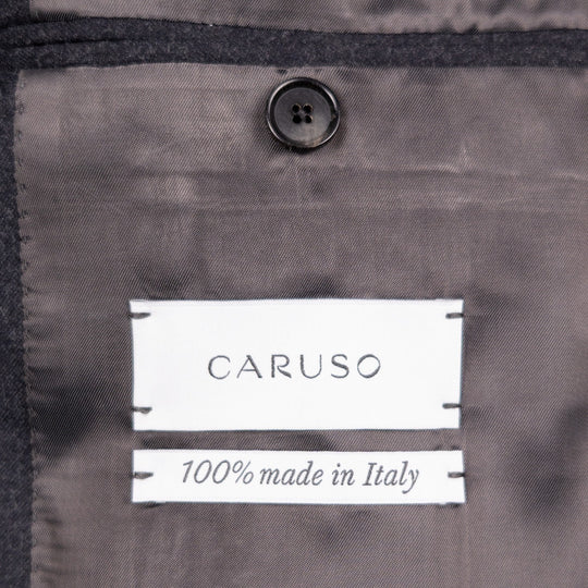 Close-up of a dark gray garment interior with a visible CARUSO label reading '100% made in Italy' and a dark button above it.