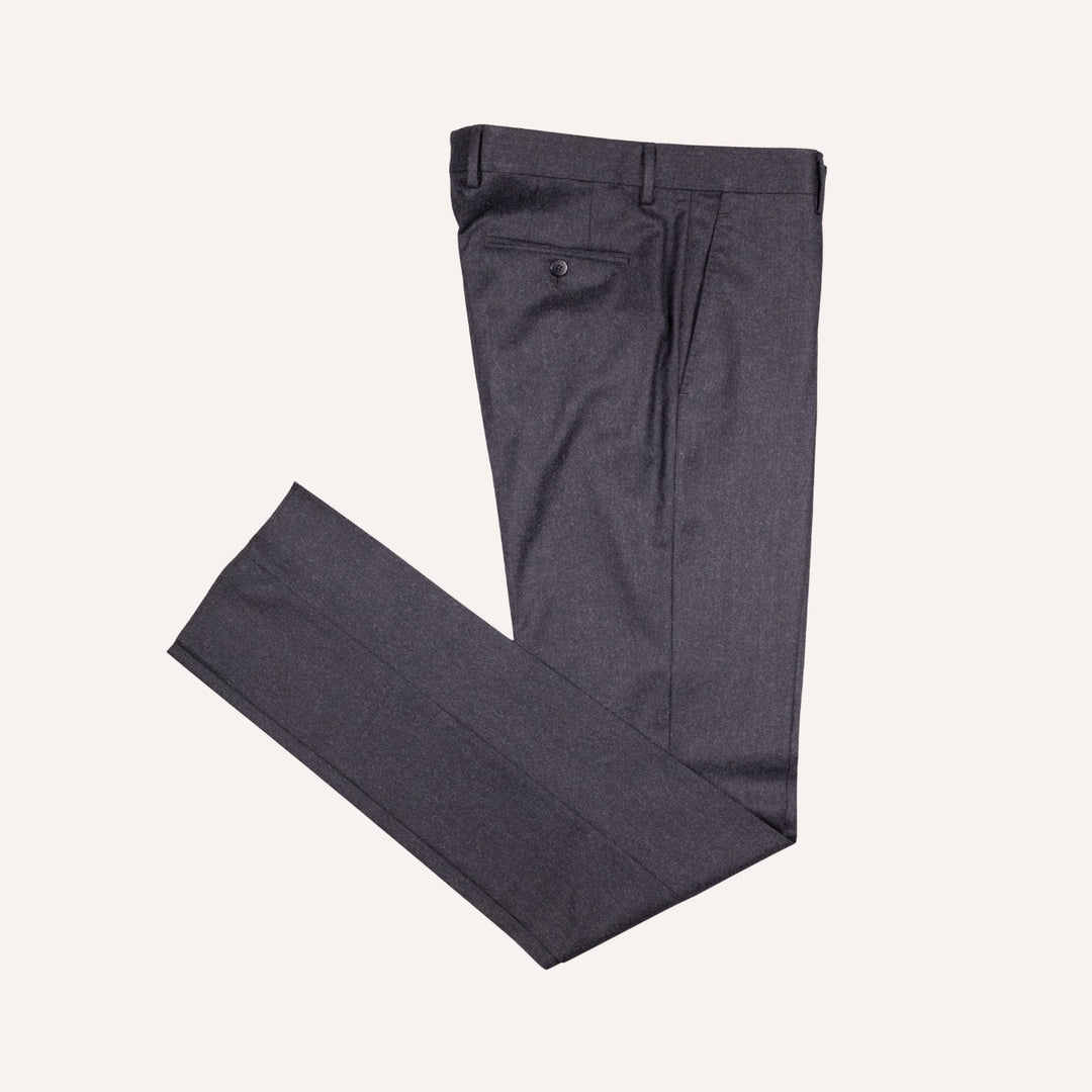 A pair of dark charcoal gray dress pants folded neatly on a light cream background.