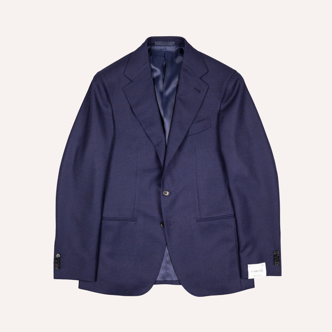 A navy blue single-breasted blazer with notch lapels, a two-button closure, and flap pockets, displayed flat against a light cream background.