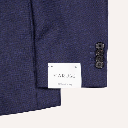 Close-up of a navy blue textured suit jacket sleeve showing three buttons on the cuff and a white brand label reading CARUSO.