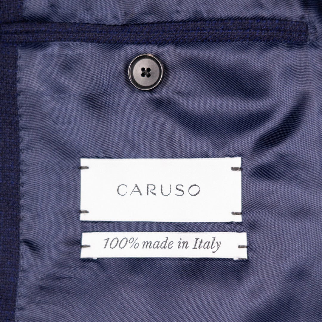 Close-up of a navy blue garment interior with a visible CARUSO label and '100% made in Italy' text, plus a dark button above.