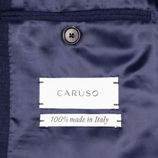 Close-up of a navy blue garment interior with a visible CARUSO label and '100% made in Italy' text, plus a dark button above.