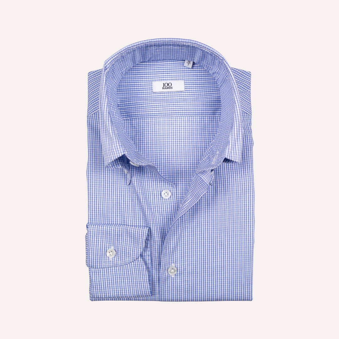 A folded light blue and white gingham dress shirt with a spread collar and button-down front, displayed on a solid off-white background.