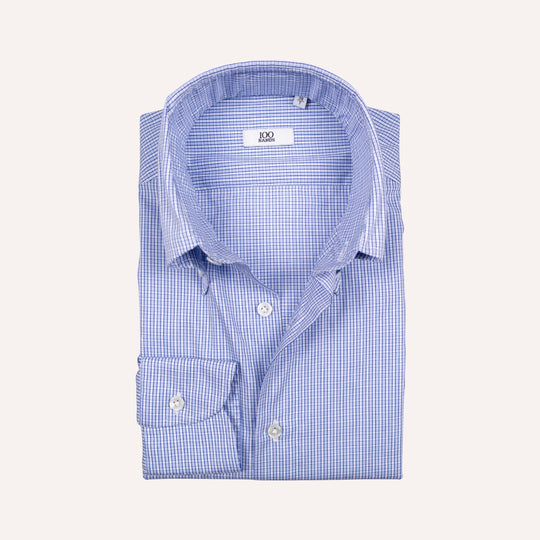 A folded light blue and white gingham dress shirt with a spread collar and button-down front, displayed on a solid off-white background.