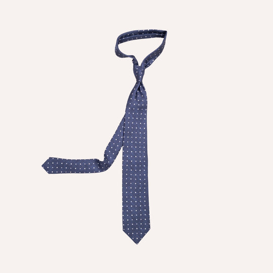 A navy blue necktie with a small white polka dot pattern, neatly arranged on a solid off-white background.