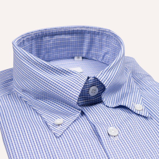 Close-up of a blue and white micro-check patterned button-down shirt collar with white buttons on a light cream background.