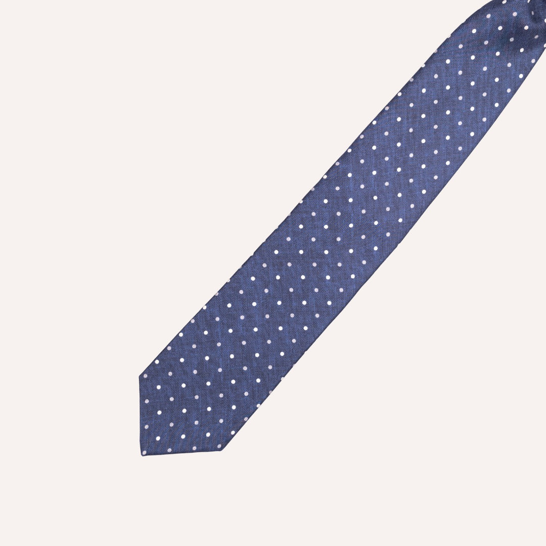 A navy blue necktie with a white polka dot pattern, laid diagonally on a light cream background.