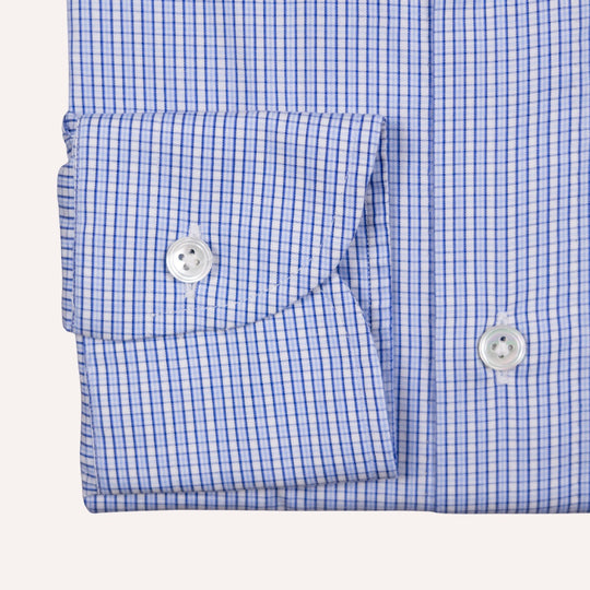 Close-up of a blue and white gingham checkered shirt cuff with a silver button, set against a light beige background.