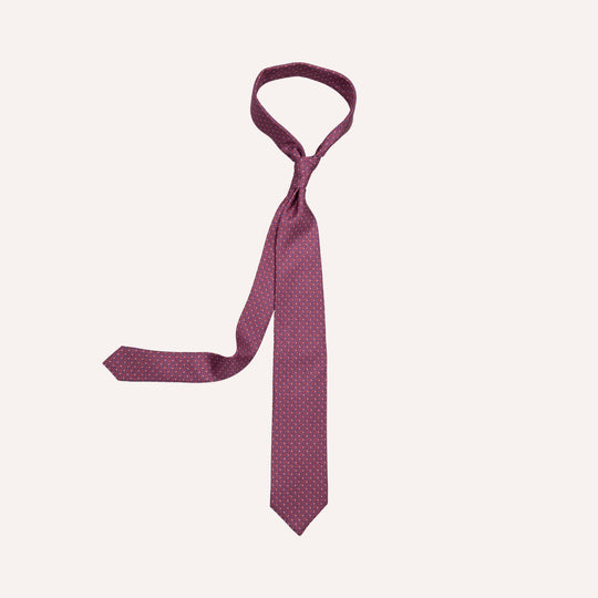 A burgundy necktie with a small repeating gold geometric pattern, shown tied in a standard knot on a light cream background.